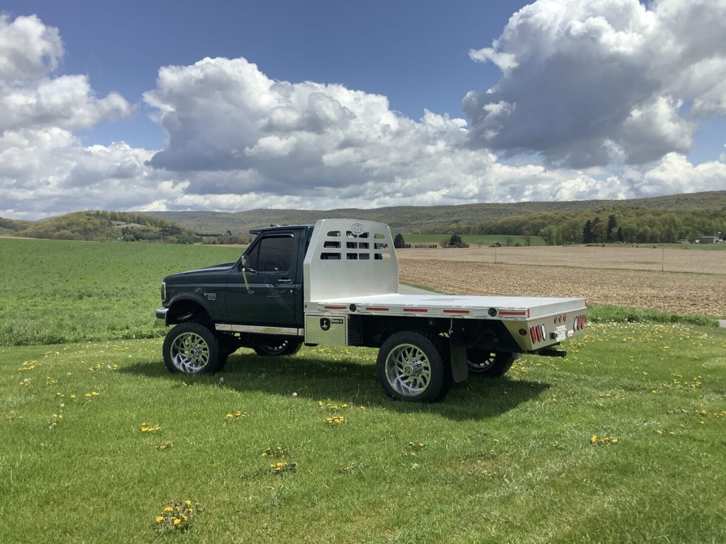 Pickup truck with a flatbed parked in a green field under a partly cloudy sky.