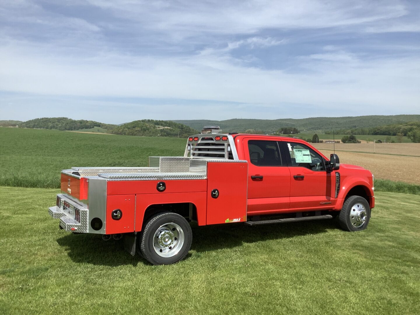 Red pickup truck with open bed storage parked in a green field with hills in the background.
