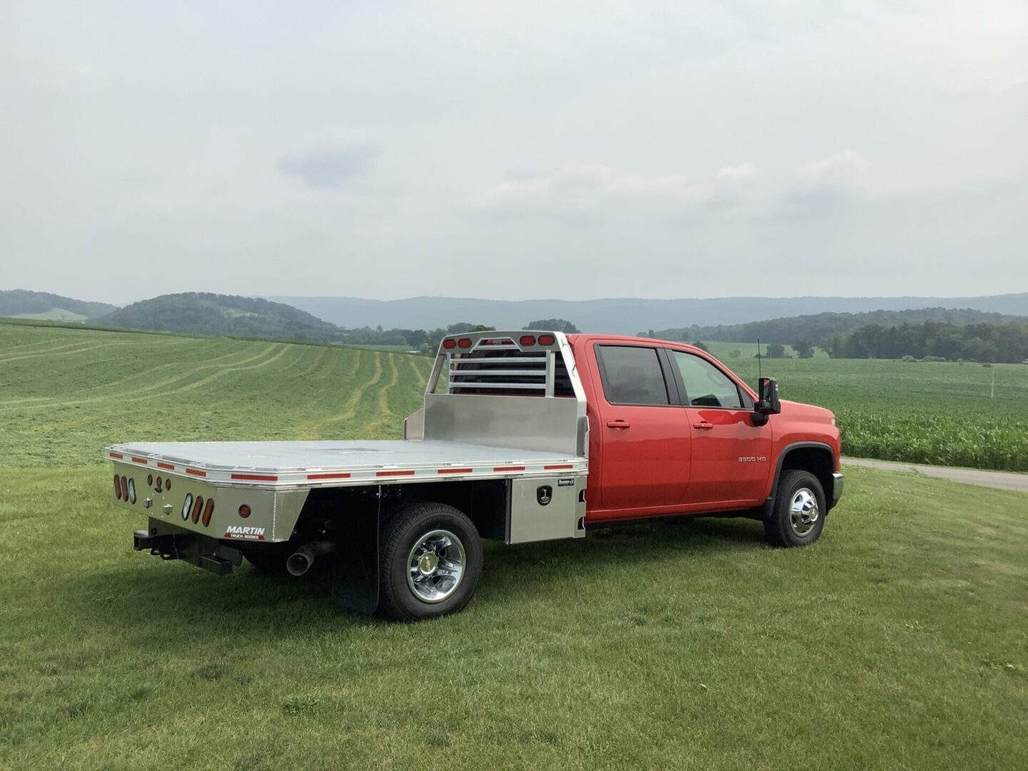 A red flatbed pickup truck parked on grass overlooking a cultivated field.